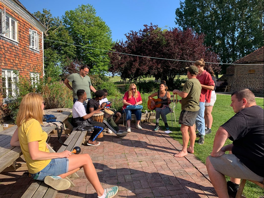 A group of people playing instruments sat outdoors in the sunshine.